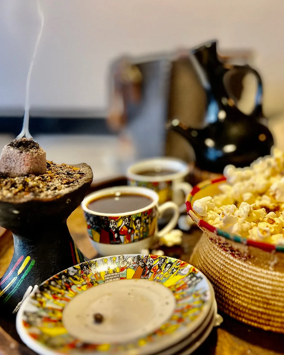 Ethiopian coffee ceremony at Zagol with a black clay jebena, hand-painted cups, a woven basket of popcorn and incense burning beside the tray