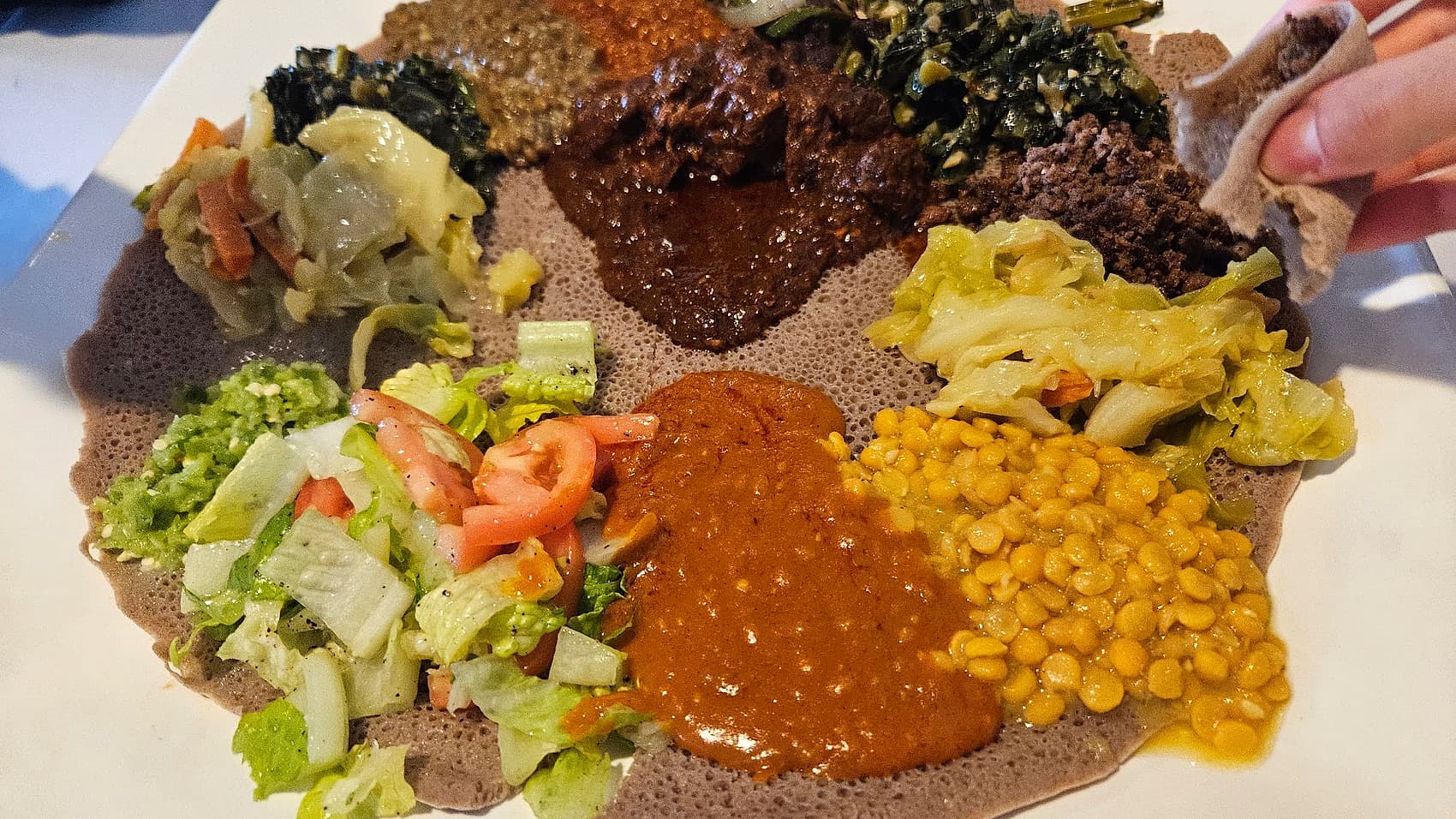 Overhead view of a full combination platter at Zagol with stews, greens, cabbage, split peas and salad on one round of injera